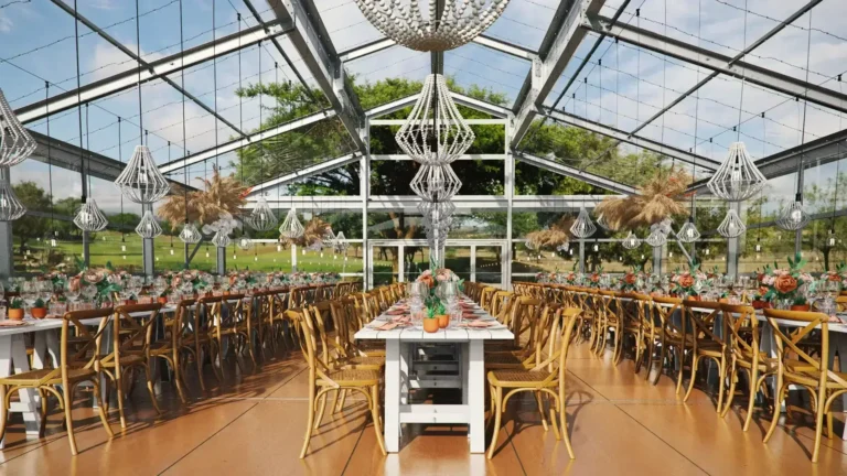 Glass frame tent with long tables, chairs, chandeliers, and event flooring for large outdoor events, weddings, and corporate parties.