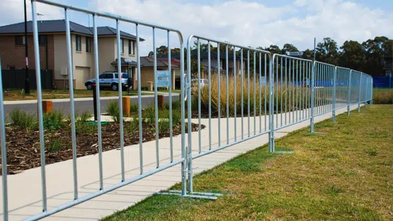 Metal crowd control barriers lined along a footpath near residential homes for public safety and event traffic management.