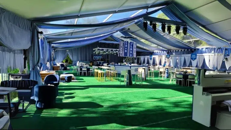 Interior of a framed event tent with blue drapery, stylish furniture, and green turf flooring.
