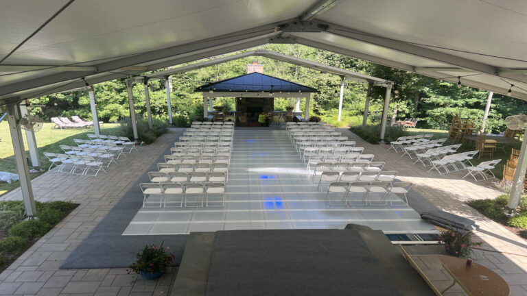 Outdoor event setup with a clear pool cover providing a stunning floor for guests, surrounded by greenery and chairs in the venue.