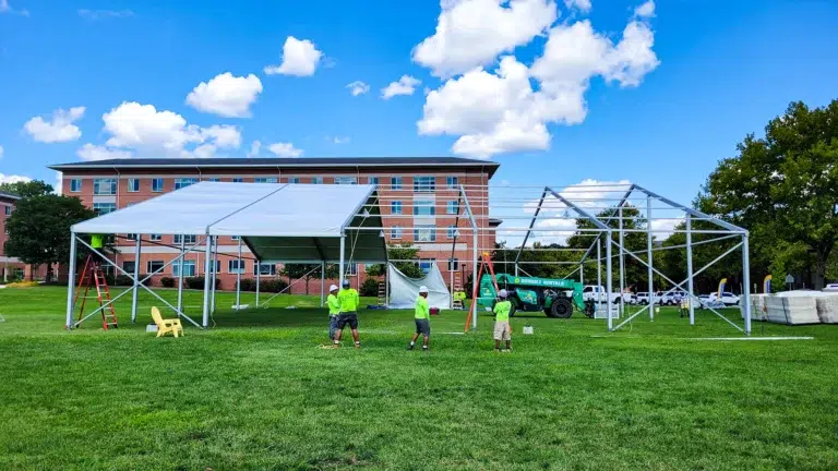 A large structure tent is being assembled on an event site, perfect for hosting large outdoor events. Workers can be seen building the frame of the tent.
