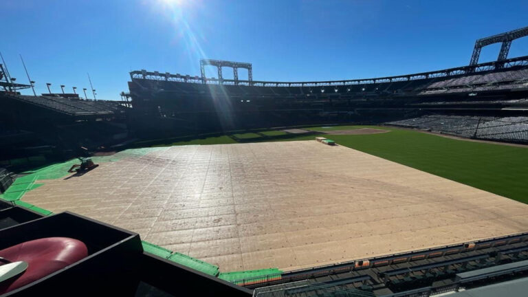 Large event flooring is placed over the grass field at a baseball stadium for turf protection during a large-scale event.