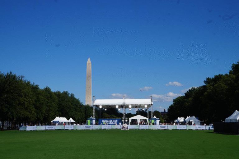 A spacious frame tent is set up outdoors, offering shelter for guests during an event. The structure is securely installed, with a well-maintained grass area and event flooring in place.