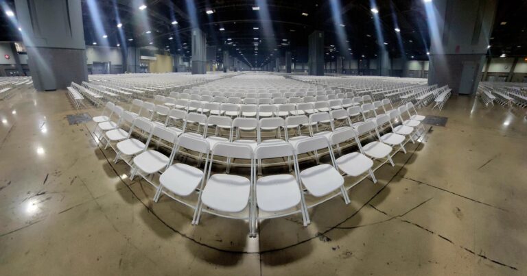 Rows of white chairs set up in a large indoor event space, prepared for a large gathering, conference, or concert with proper event seating.