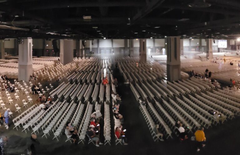 Large indoor event space with rows of white chairs set up for a significant gathering or conference, suitable for conferences, festivals, and large events.
