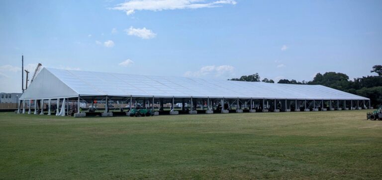 Large white frame event tent set up on a green field for an event.