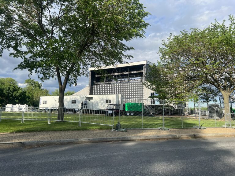 A view of an event site with perimeter fencing, temporary walkways, and event infrastructure being prepared for an upcoming gathering.