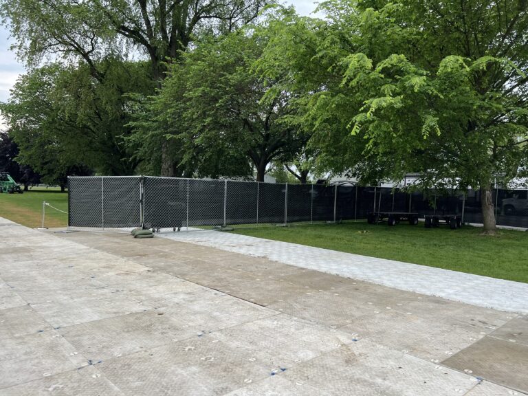 A fenced event site with large trucks parked and temporary flooring in place, providing a stable foundation for outdoor event setups.