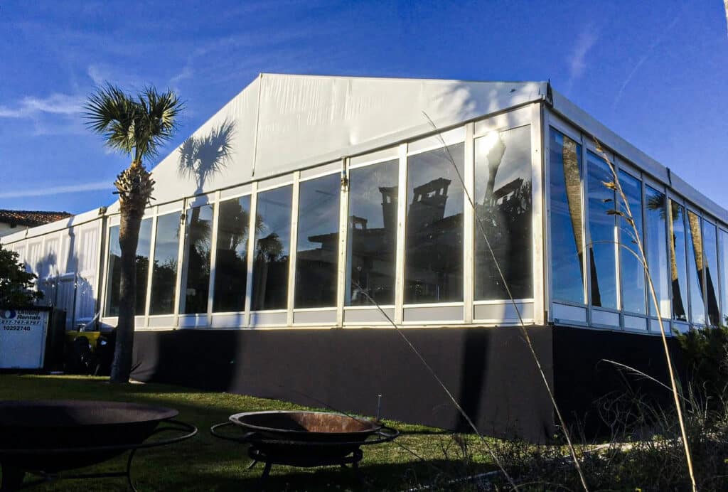 Camping and events outside can be held in a big white wall tent rental with side windows set up on green grass.
