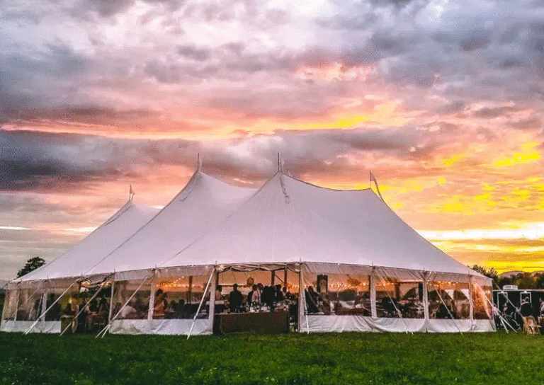 Large white Tents and Canopy setup for an outdoor wedding event at sunset with guests seated inside