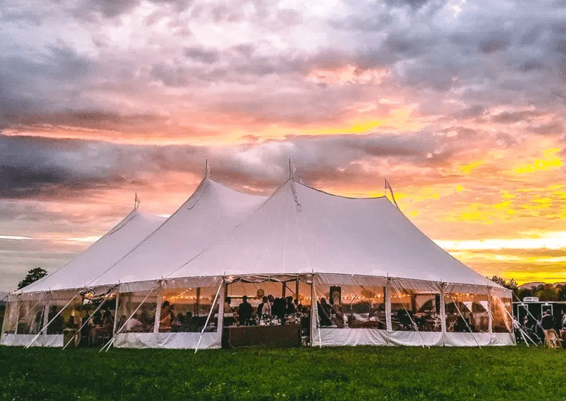 Large white Tents and Canopy setup for an outdoor wedding event at sunset with guests seated inside