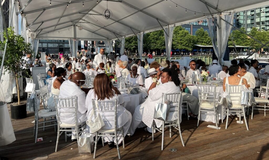 Wedding table settings arranged under a clear tent with elegant chairs, white linens, and place settings for an outdoor reception.