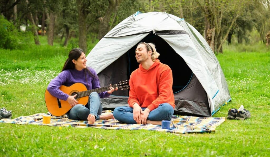 Two people relaxing outside a Decathlon tent while enjoying a guitar session during their camping trip.