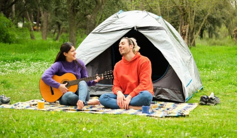 Two people relaxing outside a Decathlon tent while enjoying a guitar session during their camping trip.