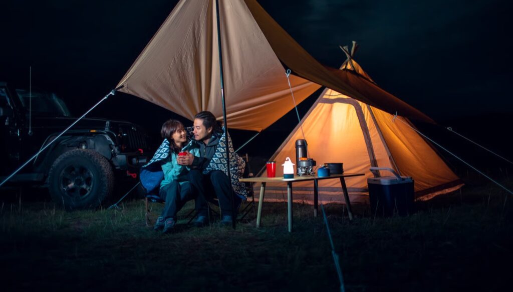Couple enjoying the warmth inside a hot tent during a nighttime camping trip, surrounded by nature.