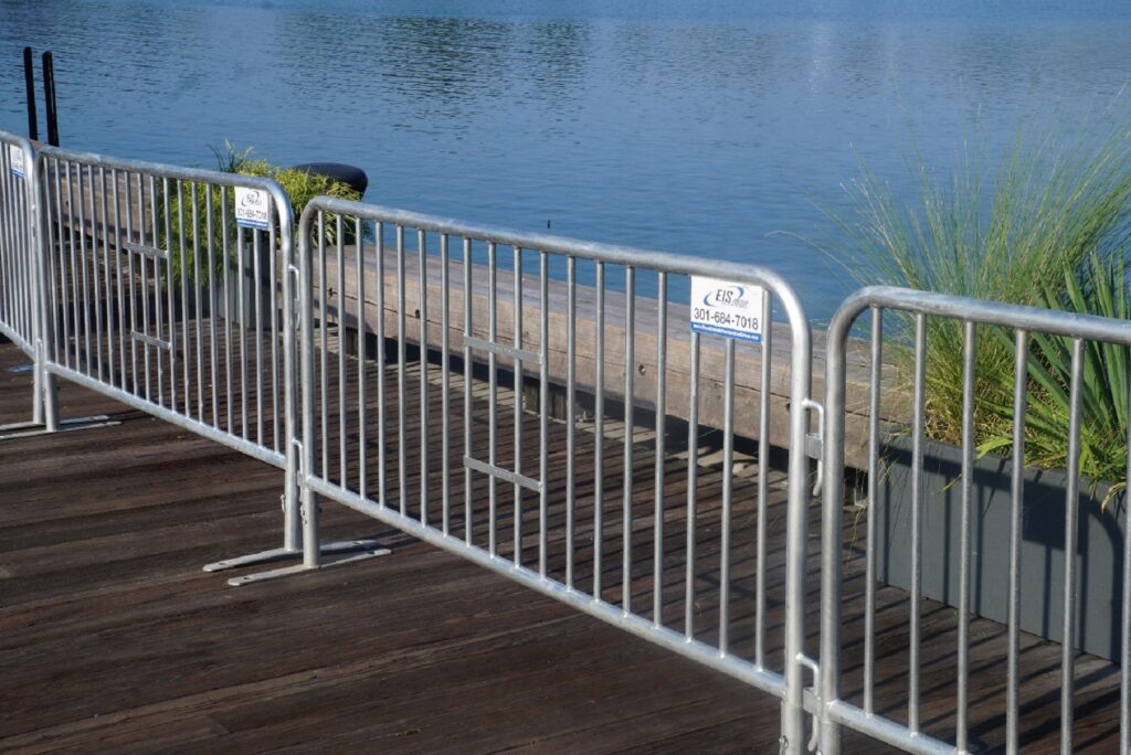 Sturdy galvanized steel barricades used for crowd control on a wooden pier near the water for event safety.