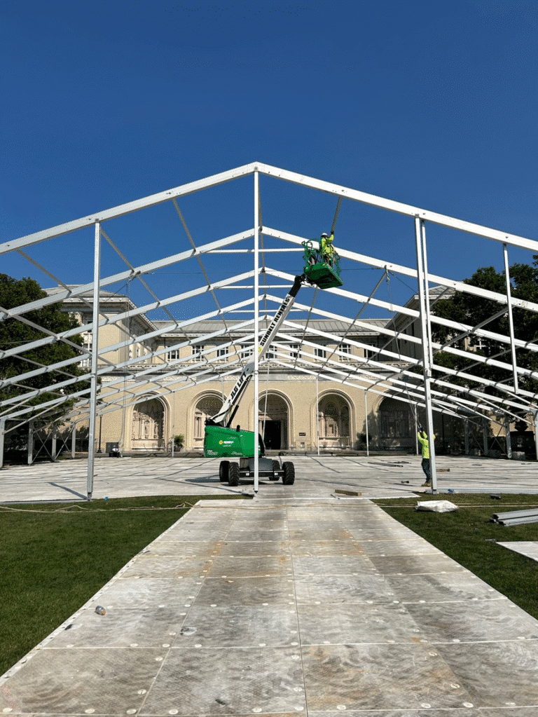 Professional installation of a large aluminum frame for a University Orientation Tent on a college campus using a boom lift.