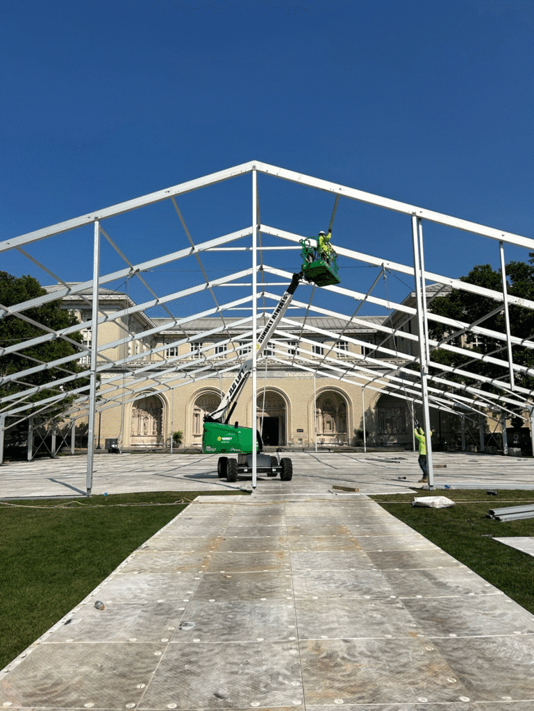 Professional installation of a large aluminum frame for a University Orientation Tent on a college campus using a boom lift.